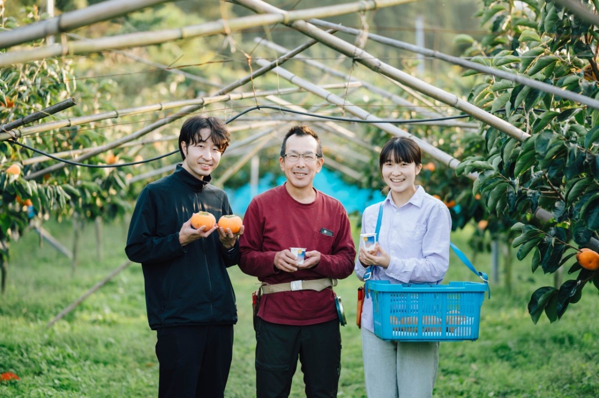 鳥取県倉吉市の福井果樹園で柿「輝太郎」を持つ生産者と『三朝ヨーグルト』のスタッフ